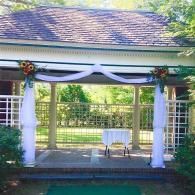 Outdoor wedding arch with white drapes and floral decorations on a patio by a pool