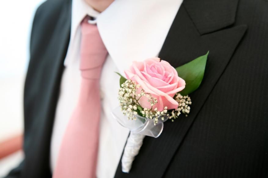 Pink rose boutonniere on a black suit with a white shirt and pink tie
