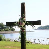 Wooden cross decorated with flowers by a lakeshore
