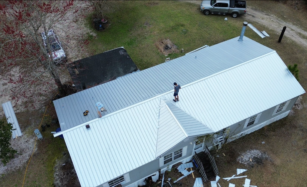 Aerial view of a white-roofed house with a person standing on the roof and a vehicle nearby.
