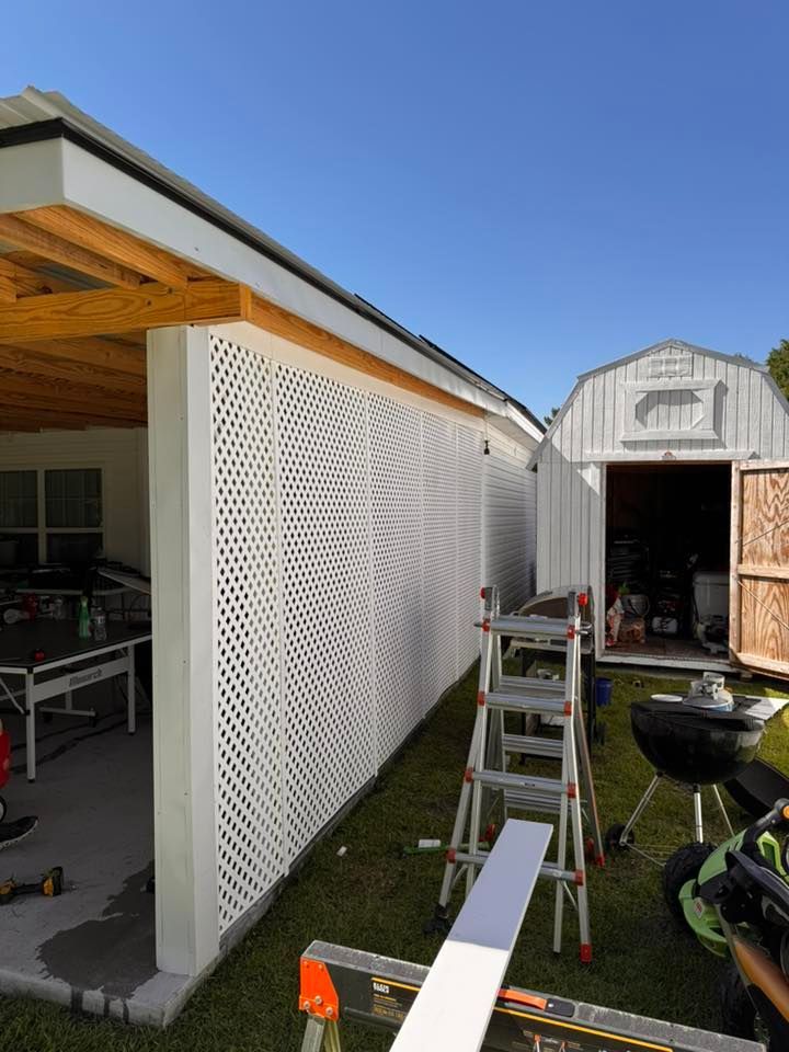 Backyard patio with white lattice panels, ladder, tools, and a shed under a clear blue sky.