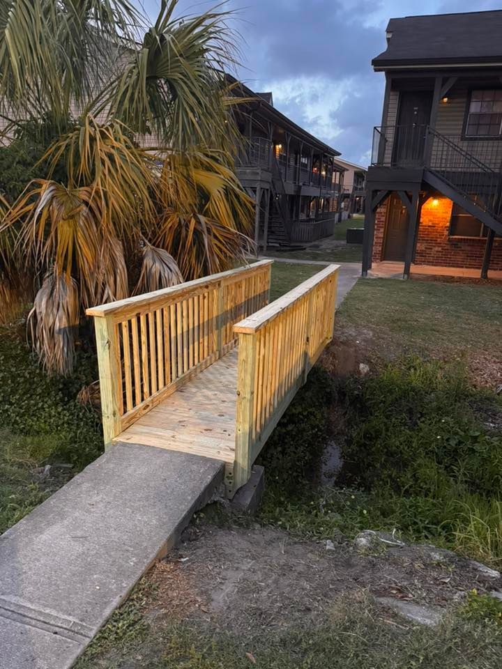 Wooden footbridge with yellow railings crossing a grassy area beside dark resort buildings at dusk.