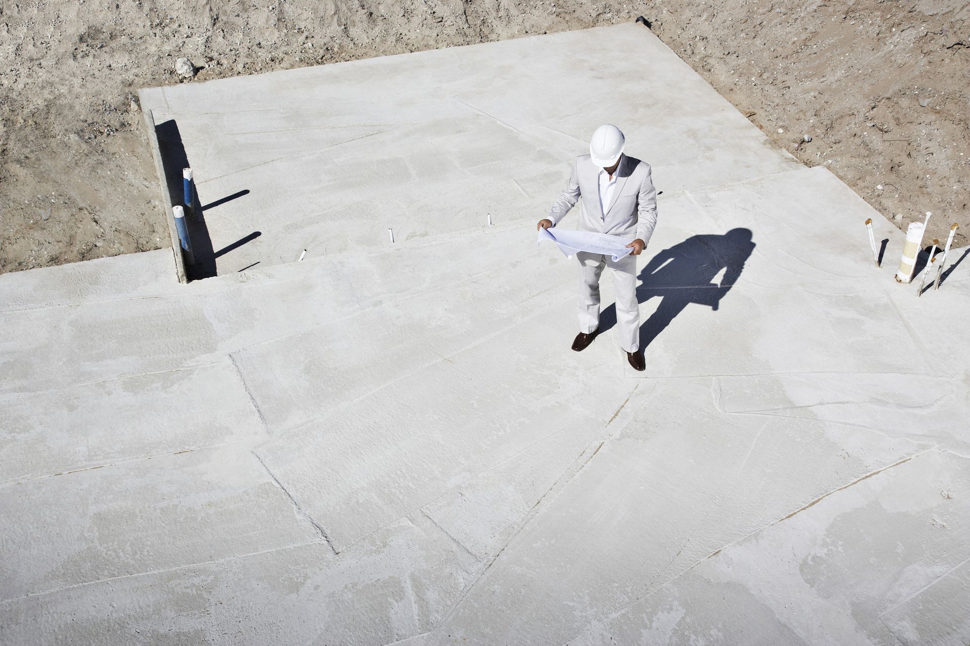 a man is standing on a concrete surface looking at a blueprint .