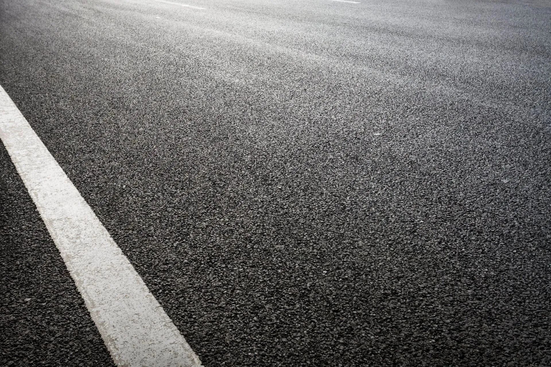 Close-up of freshly paved asphalt road with white lane markings