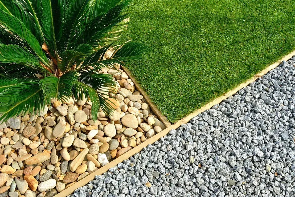 Garden corner with palm tree, lush grass, and pebbled borders.