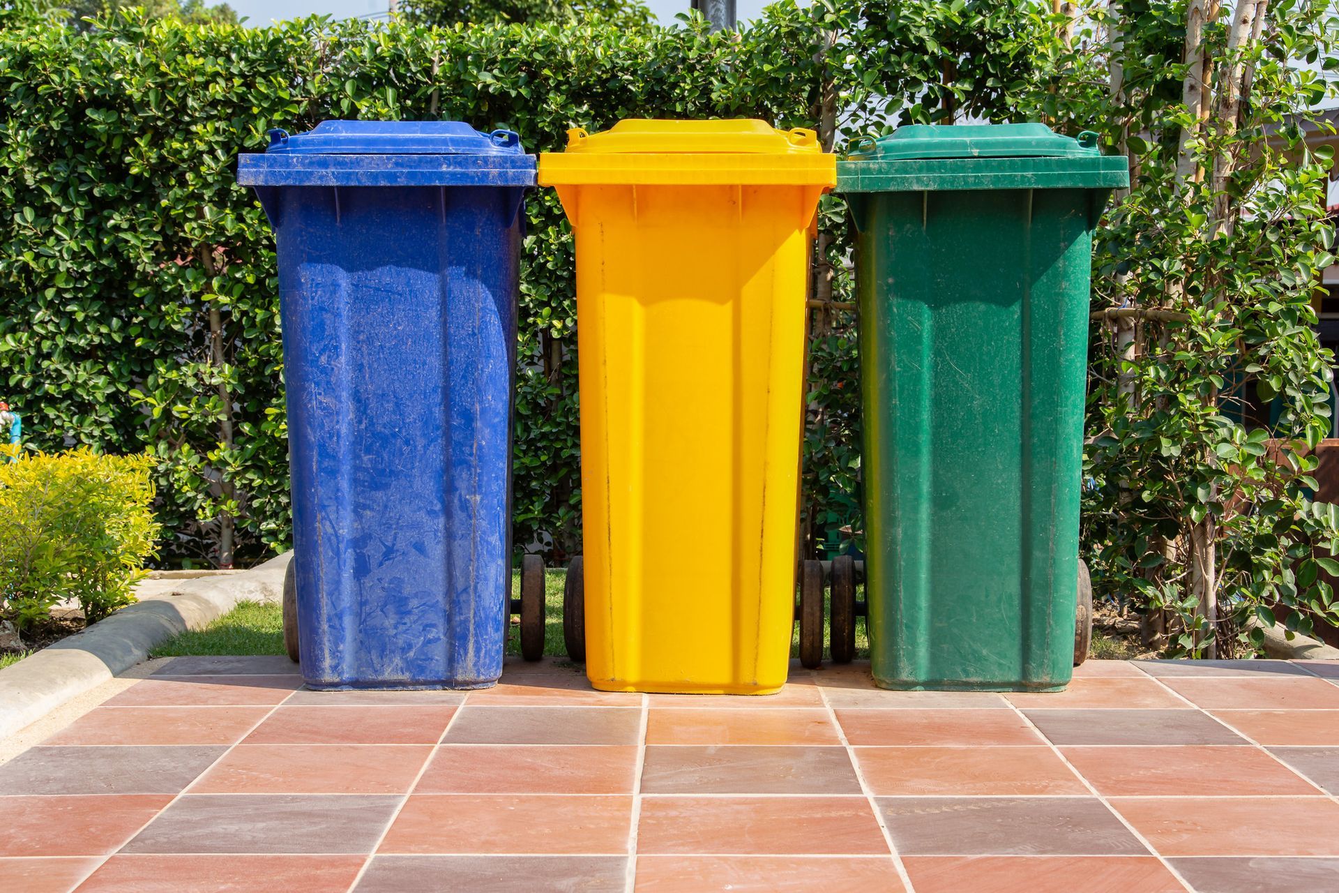 three trash cans of different colors are lined up on a tiled floor .