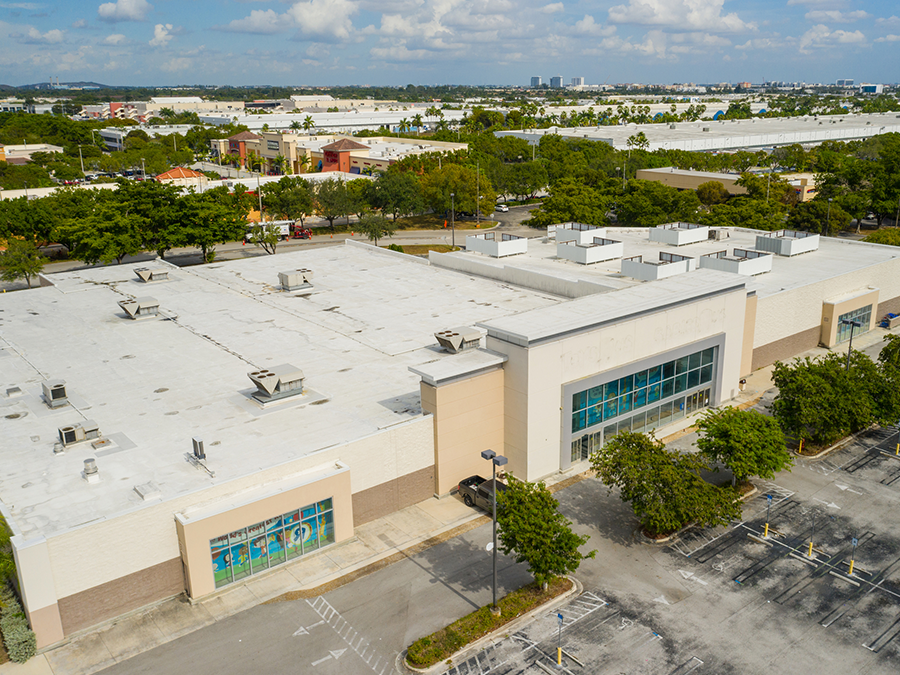 An aerial view of a large building with a white roof and a parking lot.