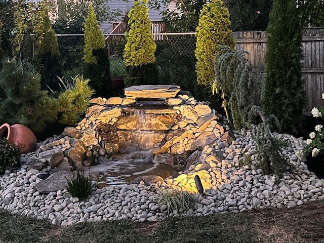 There is a waterfall in the middle of the garden surrounded by rocks and trees.