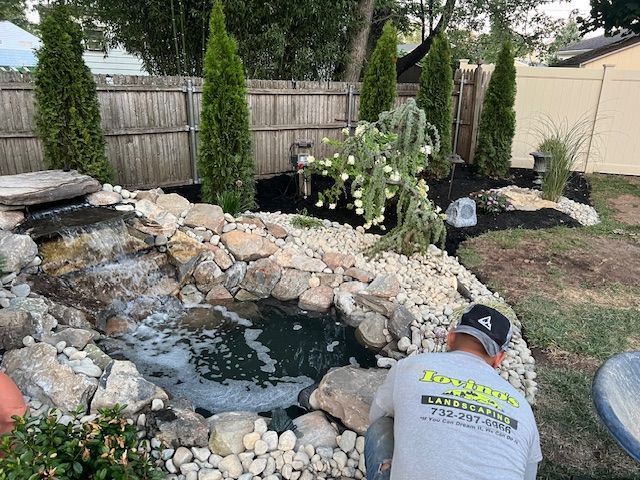 A man is working on a pond in a backyard.