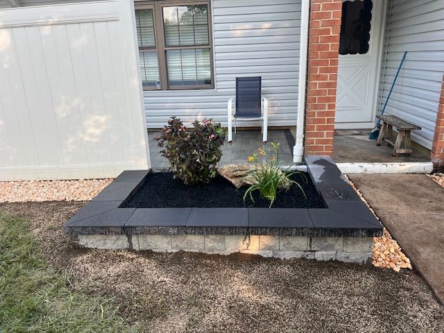 A planter with plants in it is in front of a house.