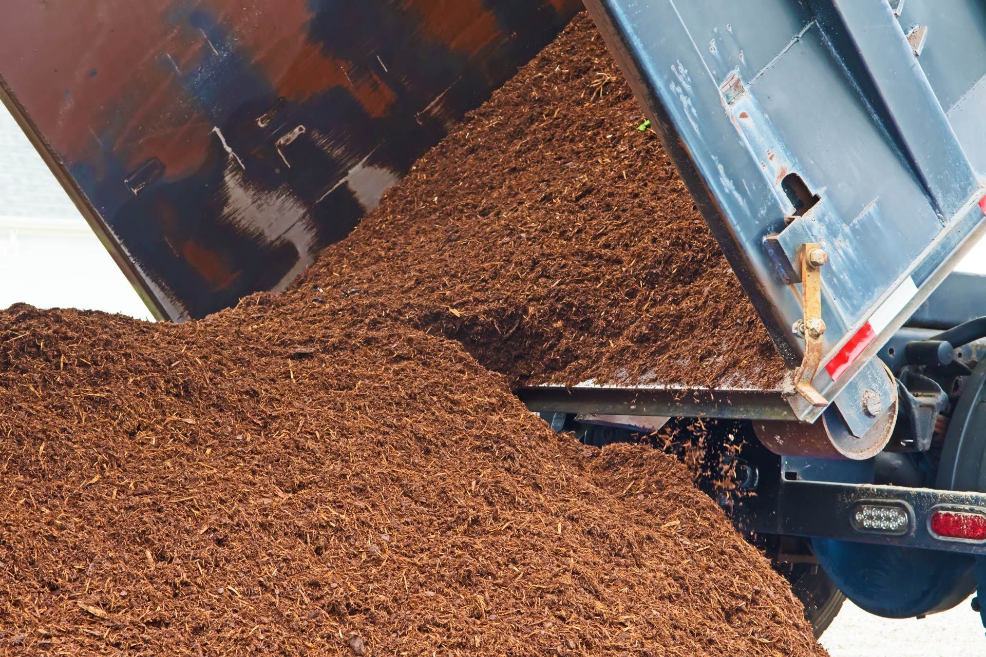 Brown mulch spilling from the raised bed of a dump truck.
