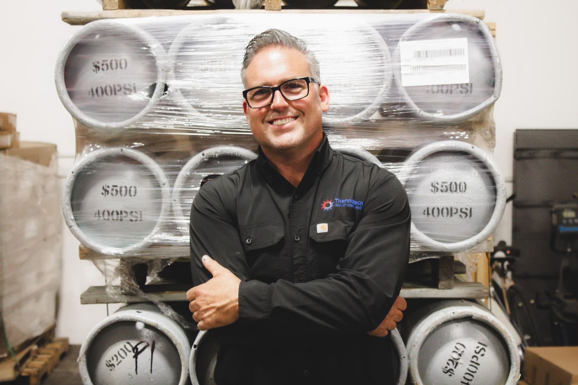 A man is standing in front of a stack of kegs.