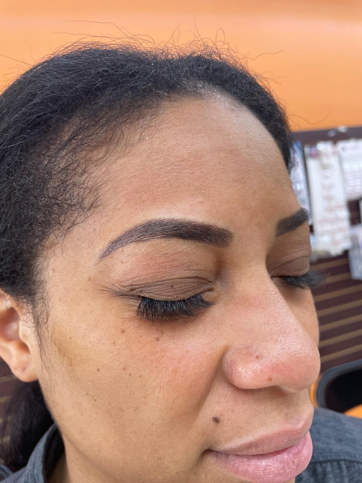 Woman with closed eyes, eyebrow tattoo, and dark lashes. Orange background.