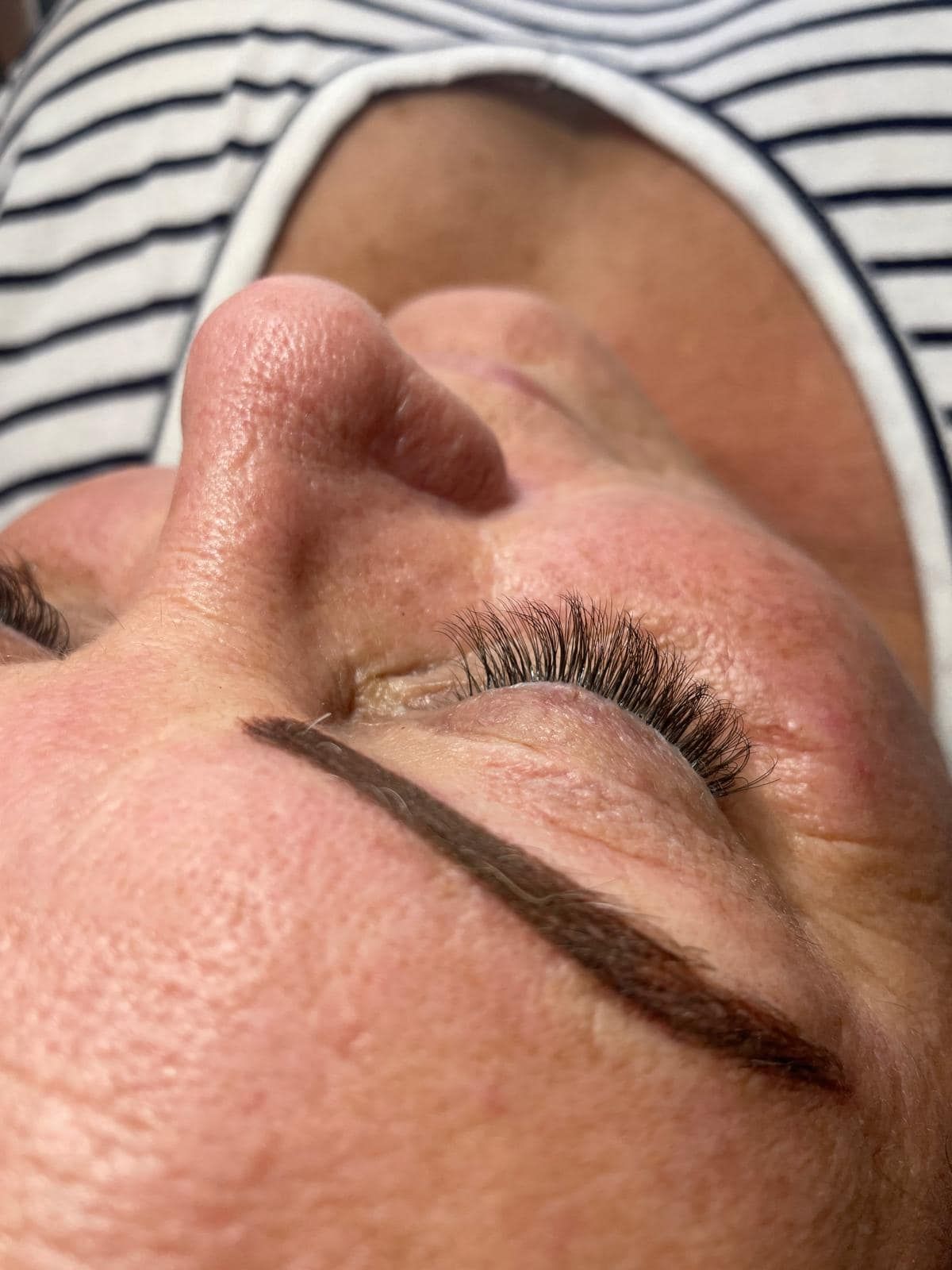 Close-up of a person's eye with a freshly tattooed eyebrow and closed eyelashes, angled view.