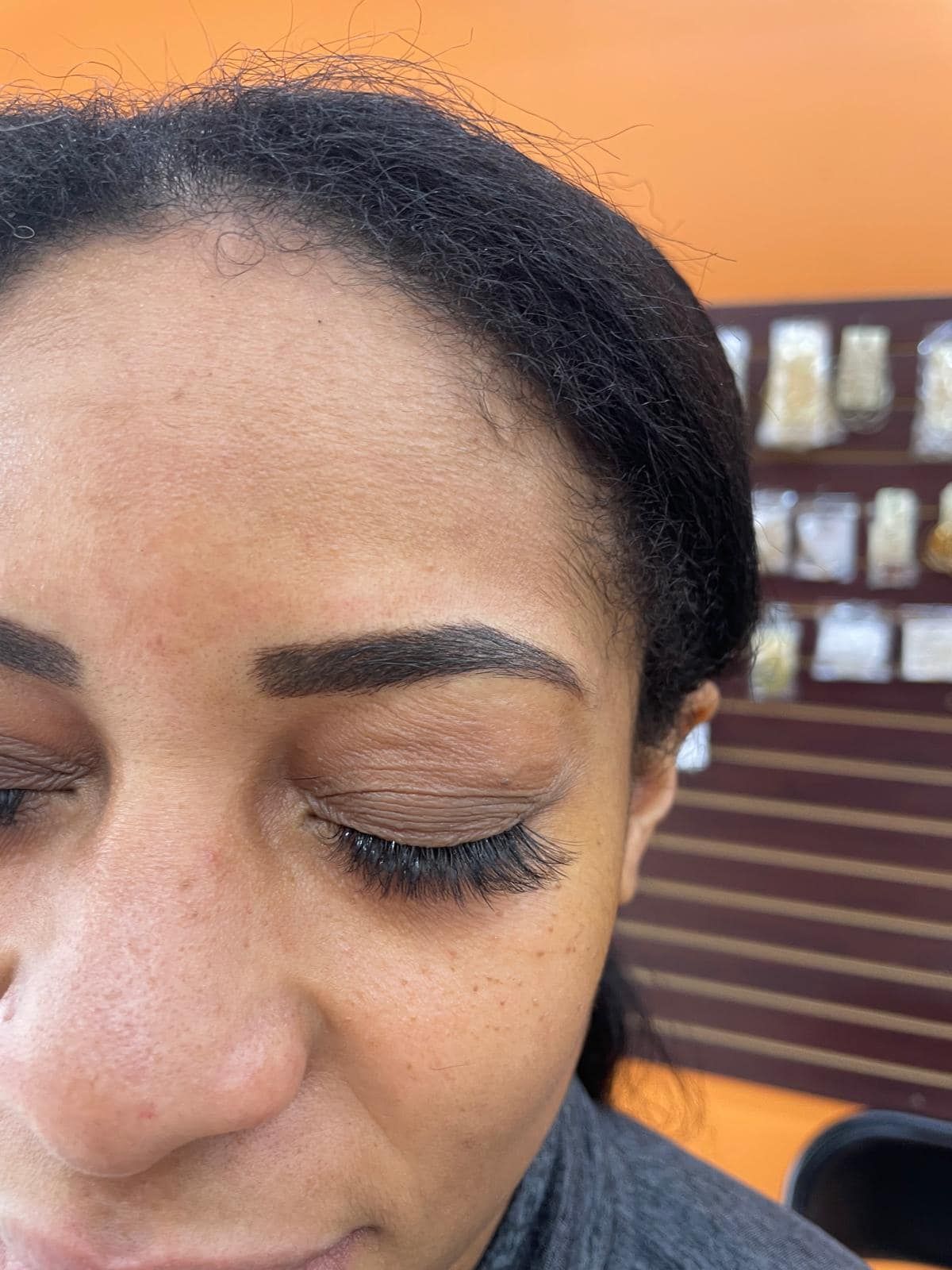 Woman with closed eyes, dark eyebrows, and long lashes. Against an orange wall background.
