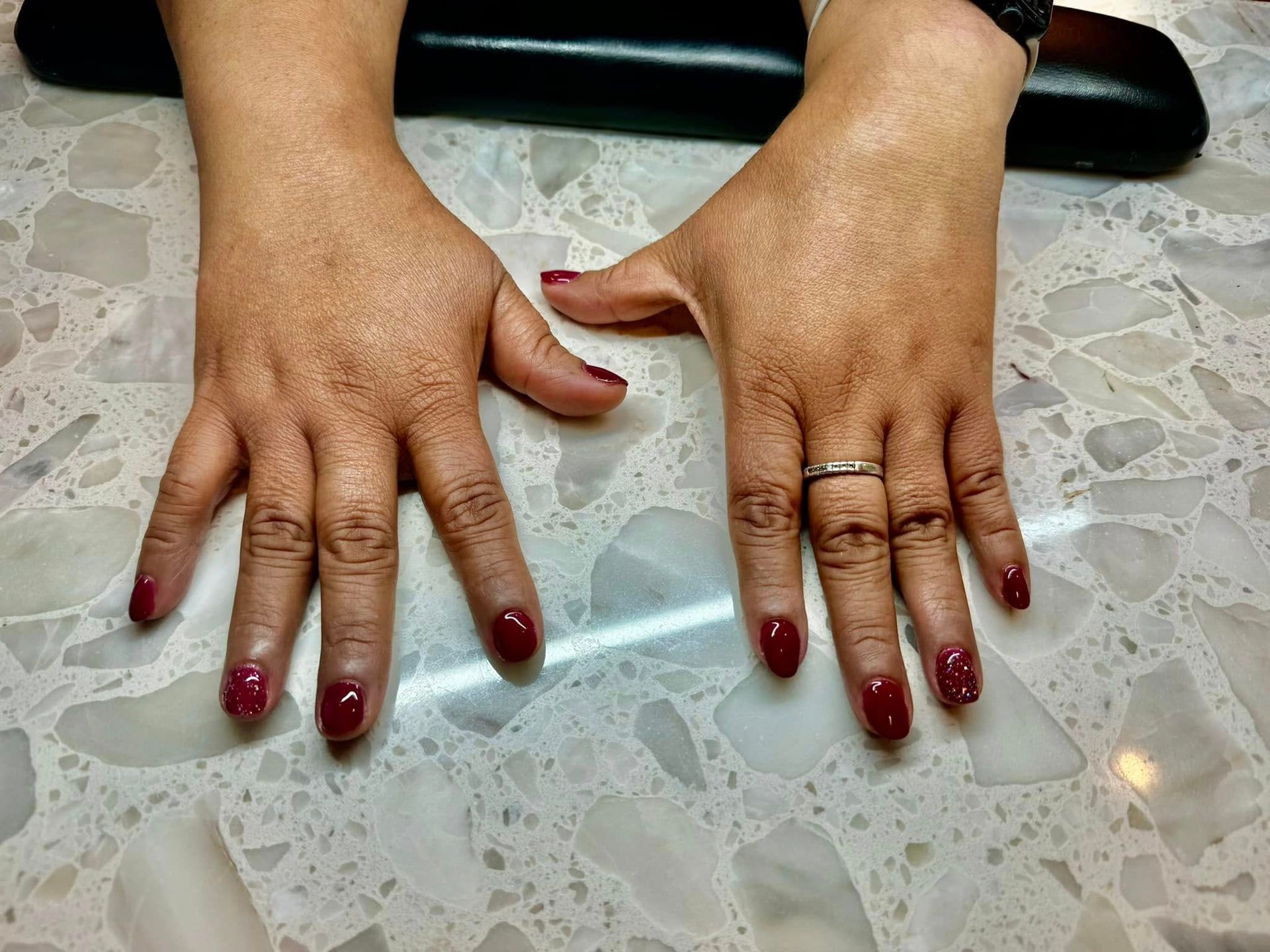 Hands with burgundy nail polish on a speckled countertop. One hand is holding an item.
