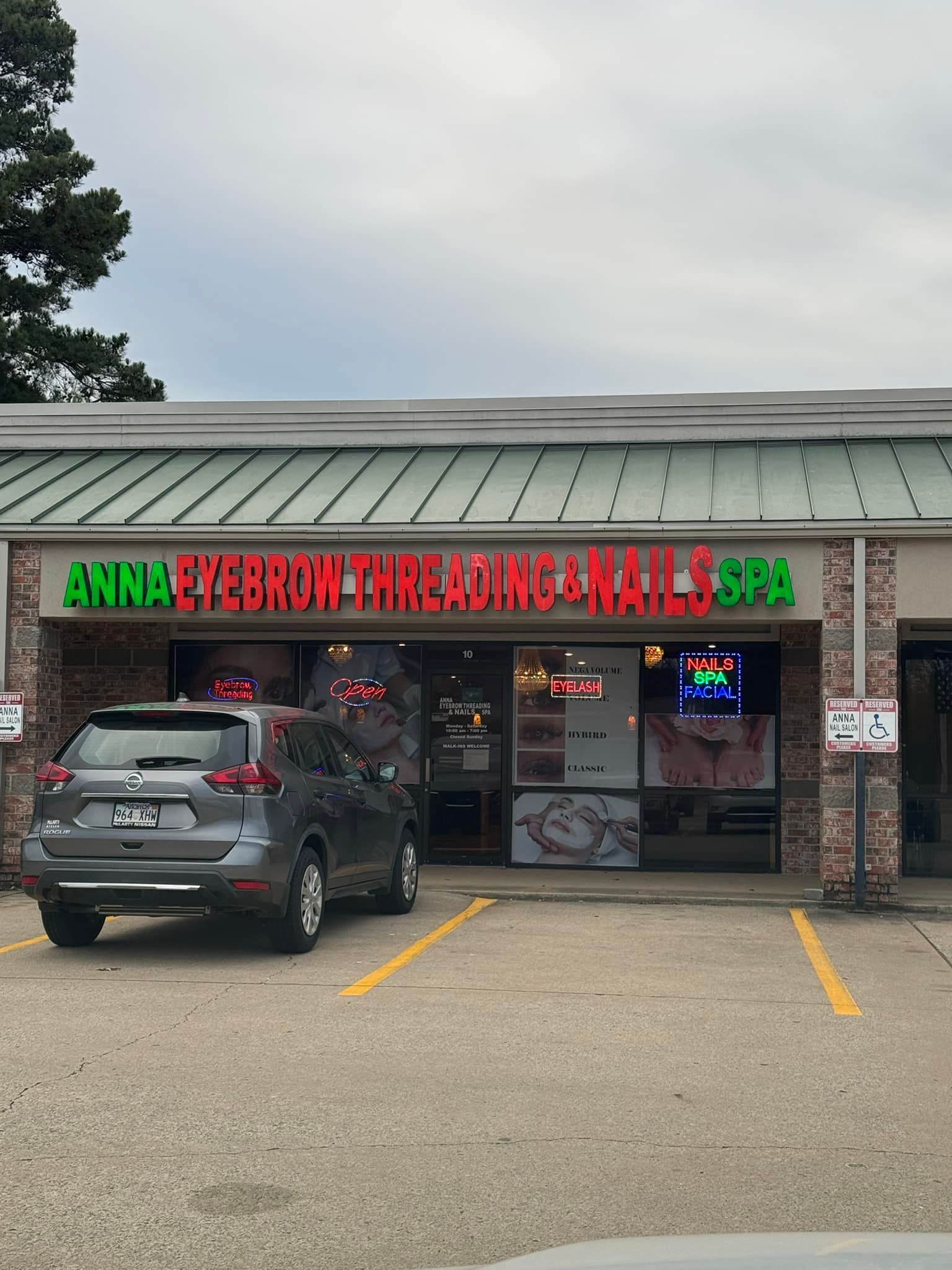 Exterior of Anna International Threading & Nail Spa. Grey SUV parked in front. Red and green signage.