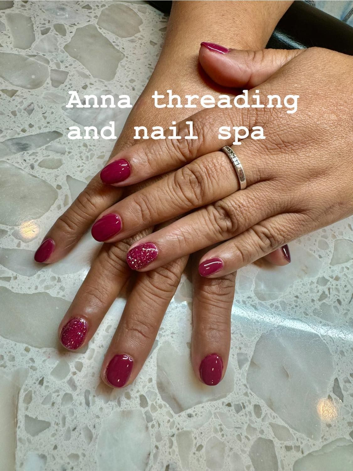 Hands with oval-shaped, red nails, one with glitter, on a patterned surface. Text: 