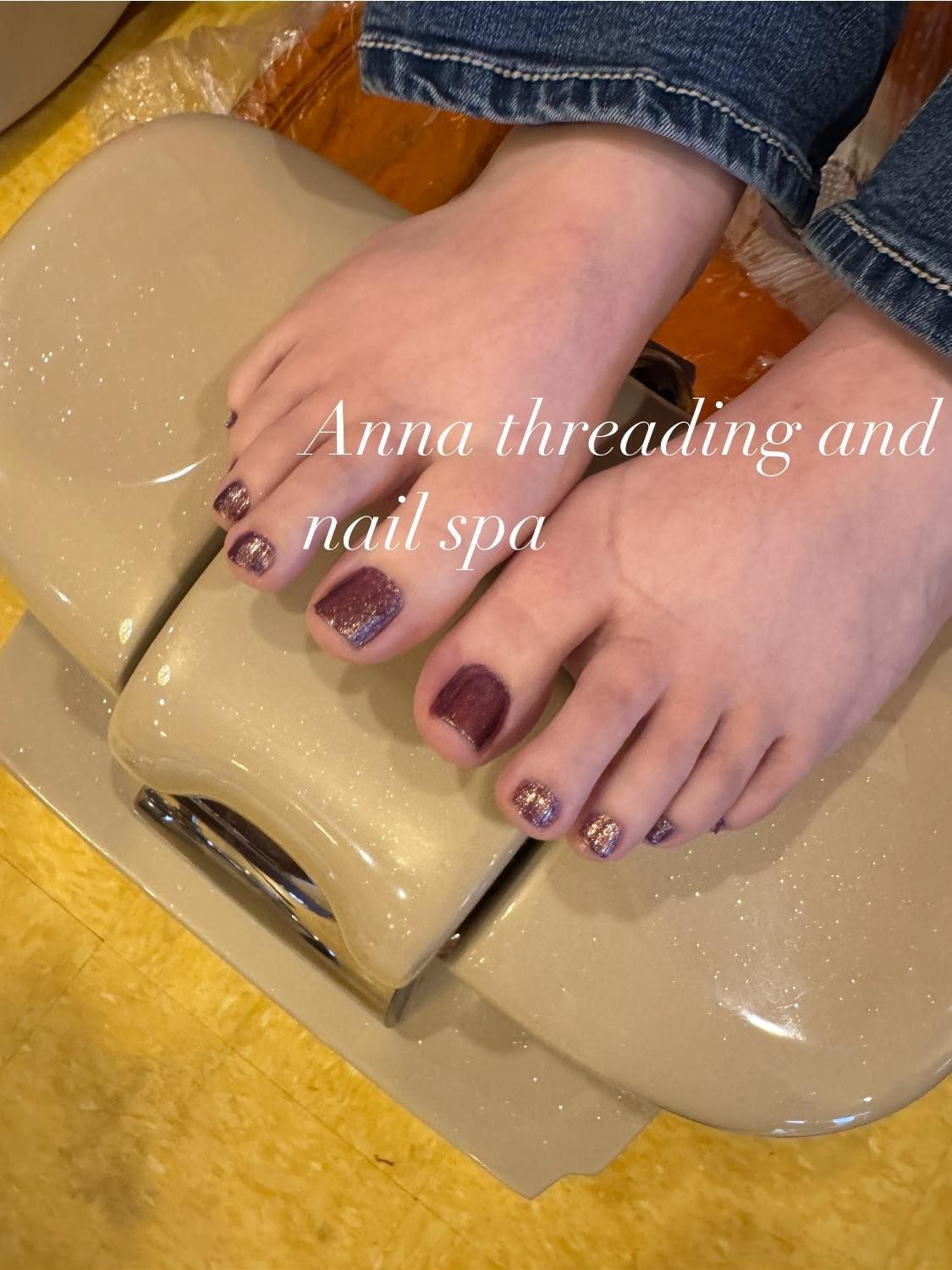 Feet with dark purple nail polish at Anna threading and nail spa.