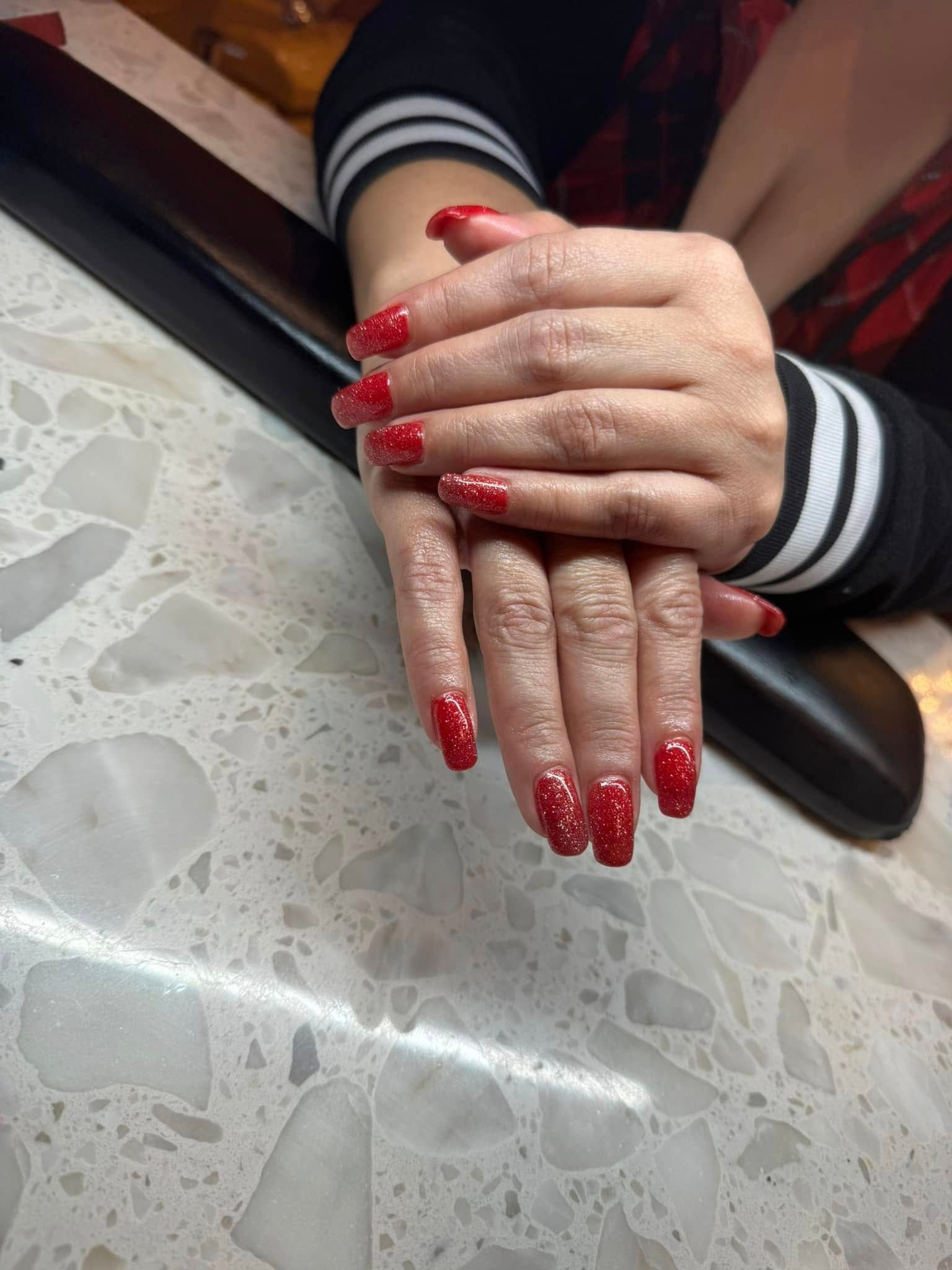 Hands with red glitter nail polish resting on a speckled surface.