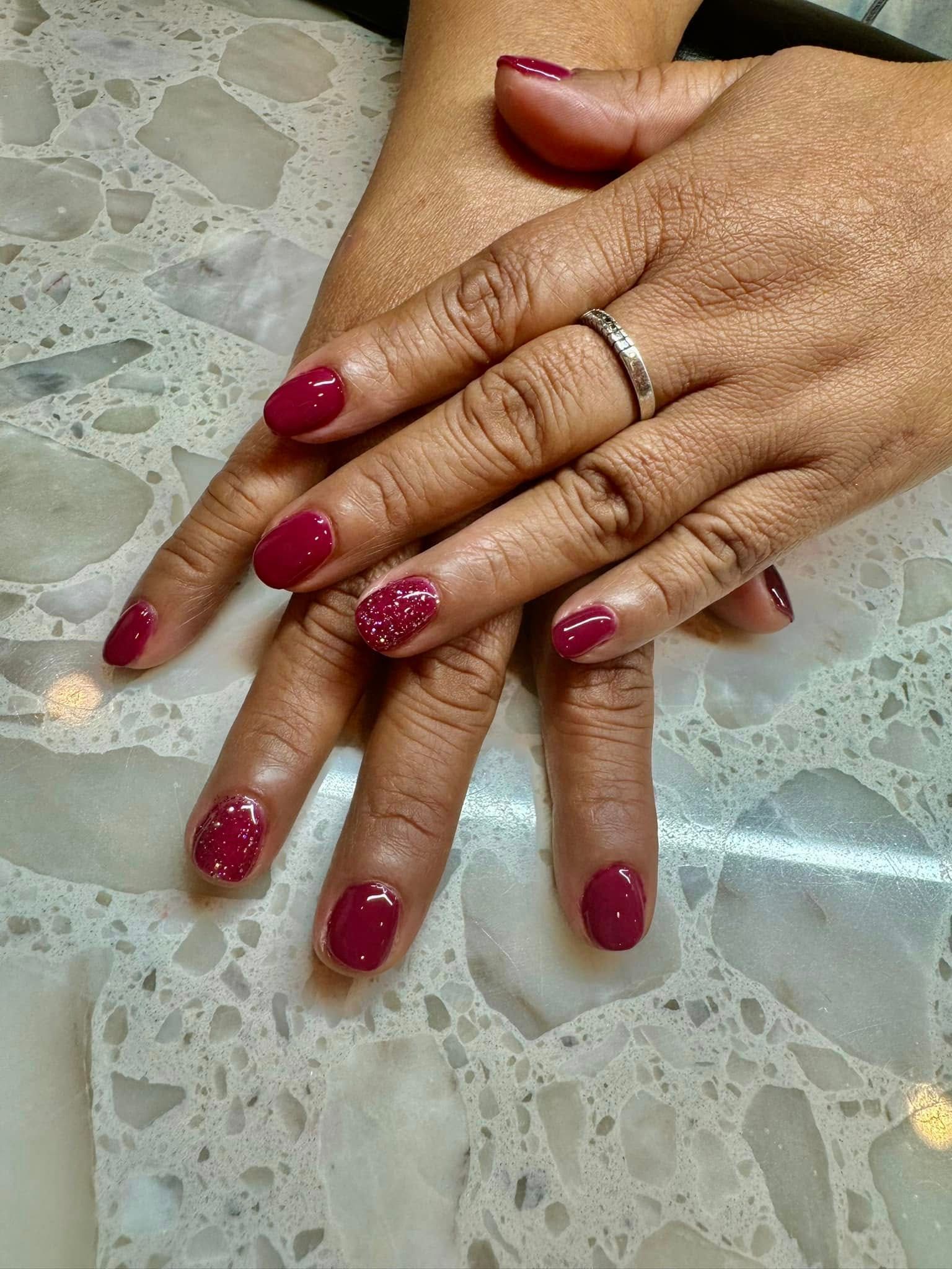 Hands with burgundy nail polish on a marbled surface. One hand has a ring.