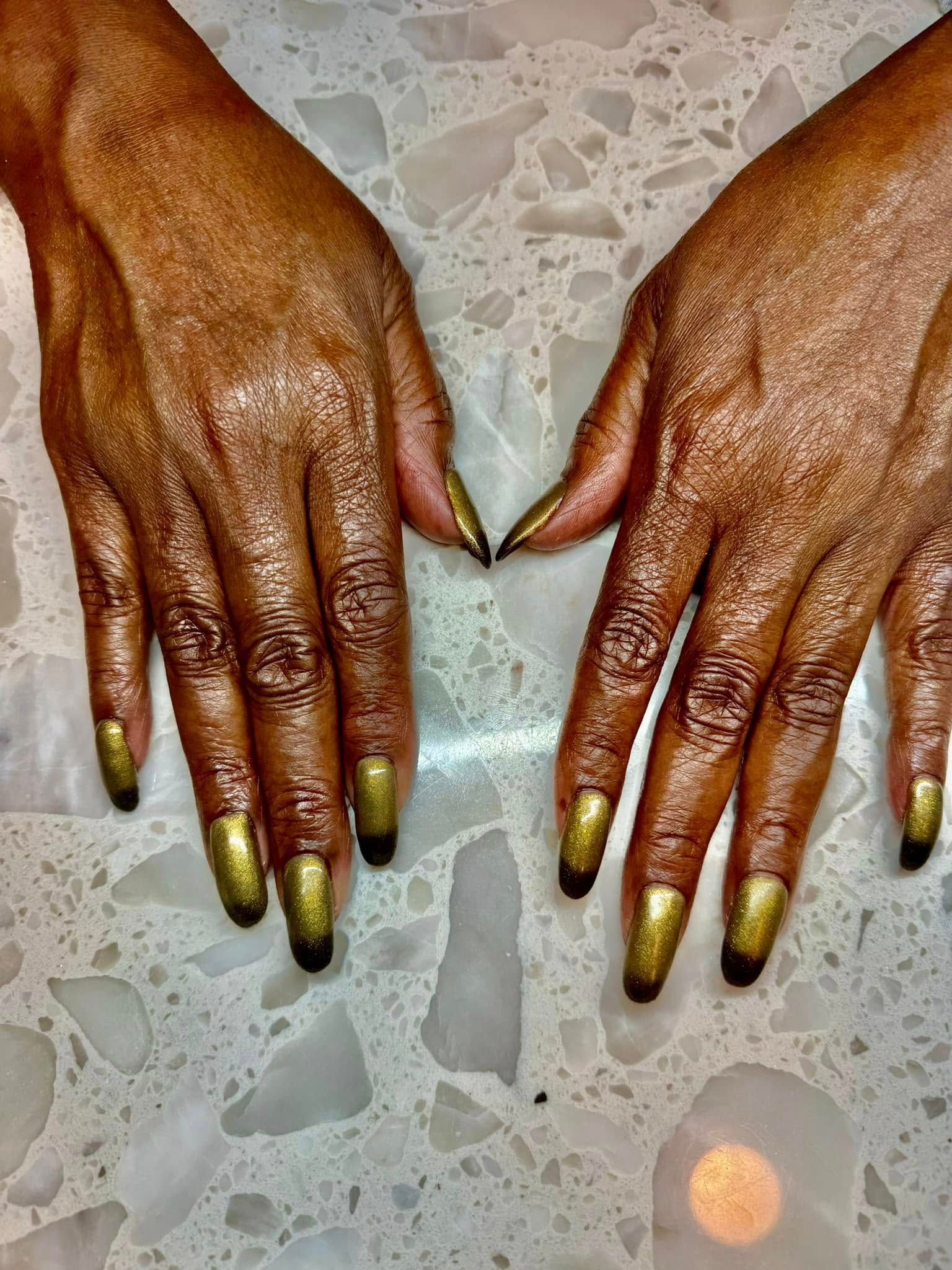 Hands with gold and black painted nails on a light, speckled surface.