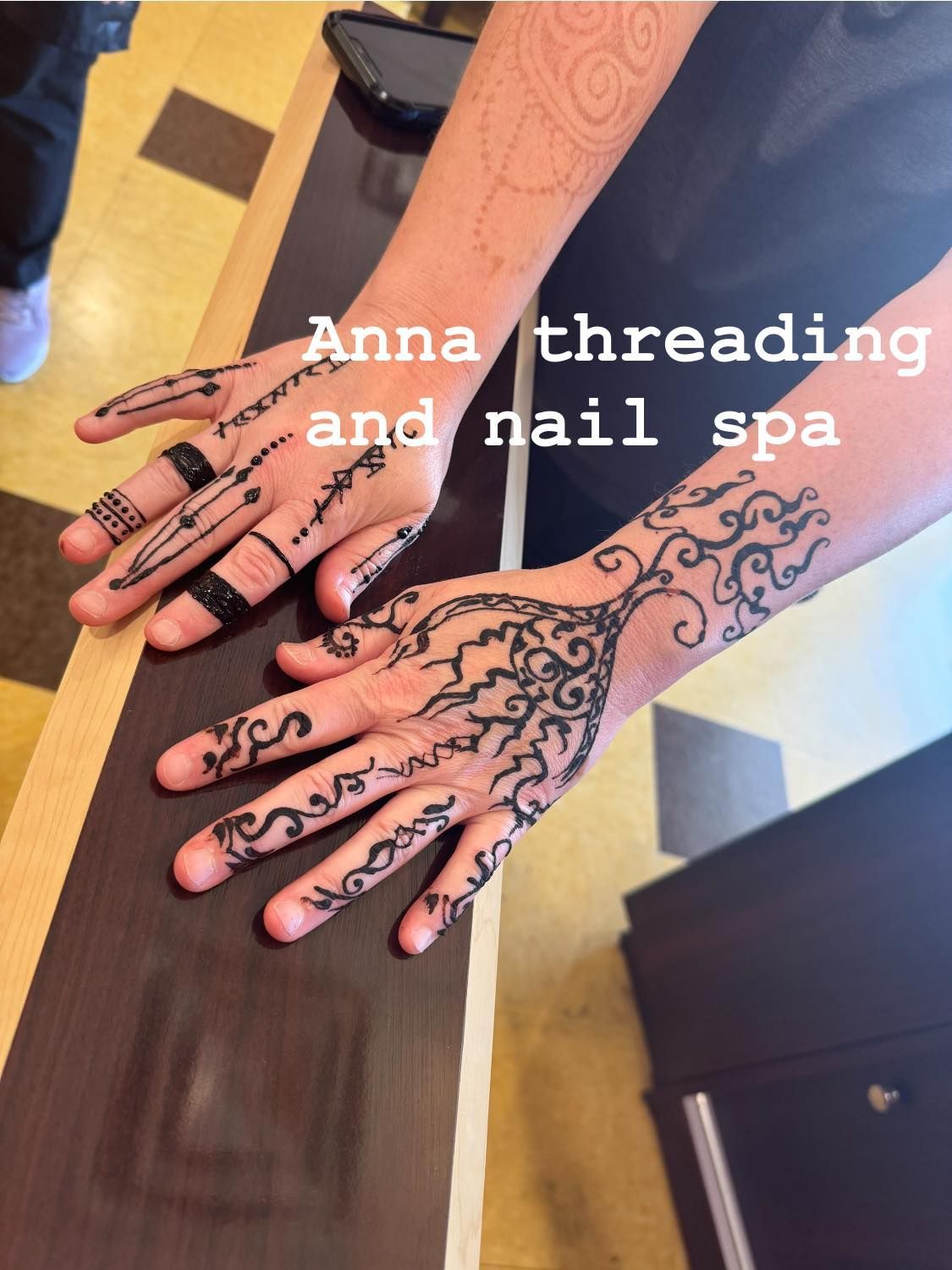 Two hands with black henna art on a dark surface. Text reads 