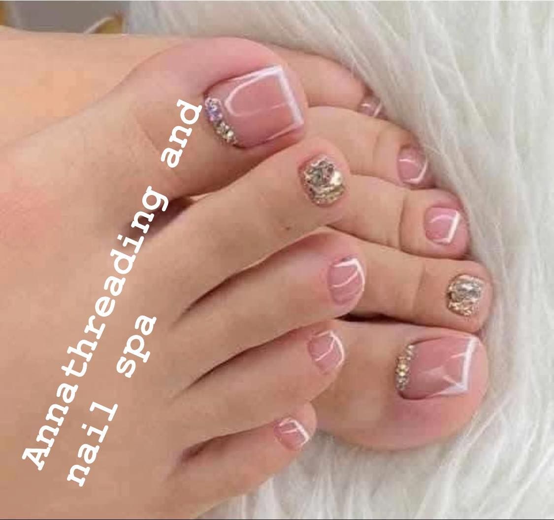 Pedicured feet with French tips, gold glitter accents, and bedazzled toes.