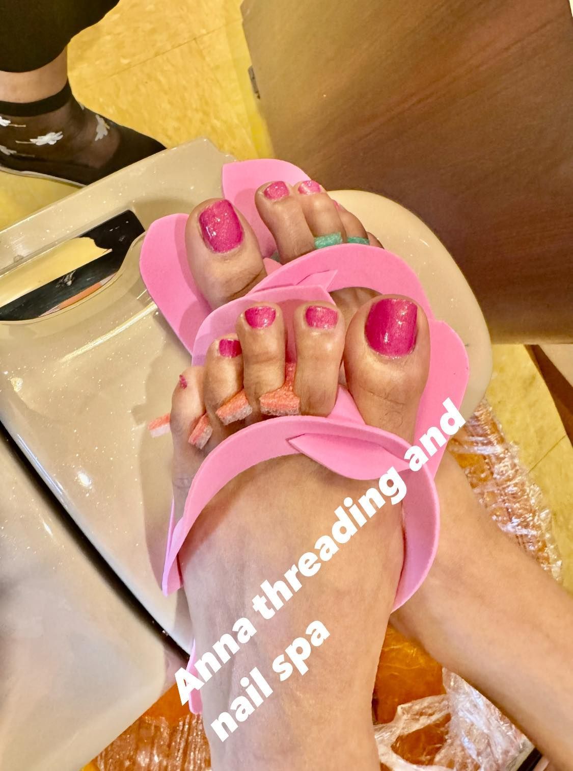 Feet with bright pink toenail polish, in a pedicure spa with toe separators.