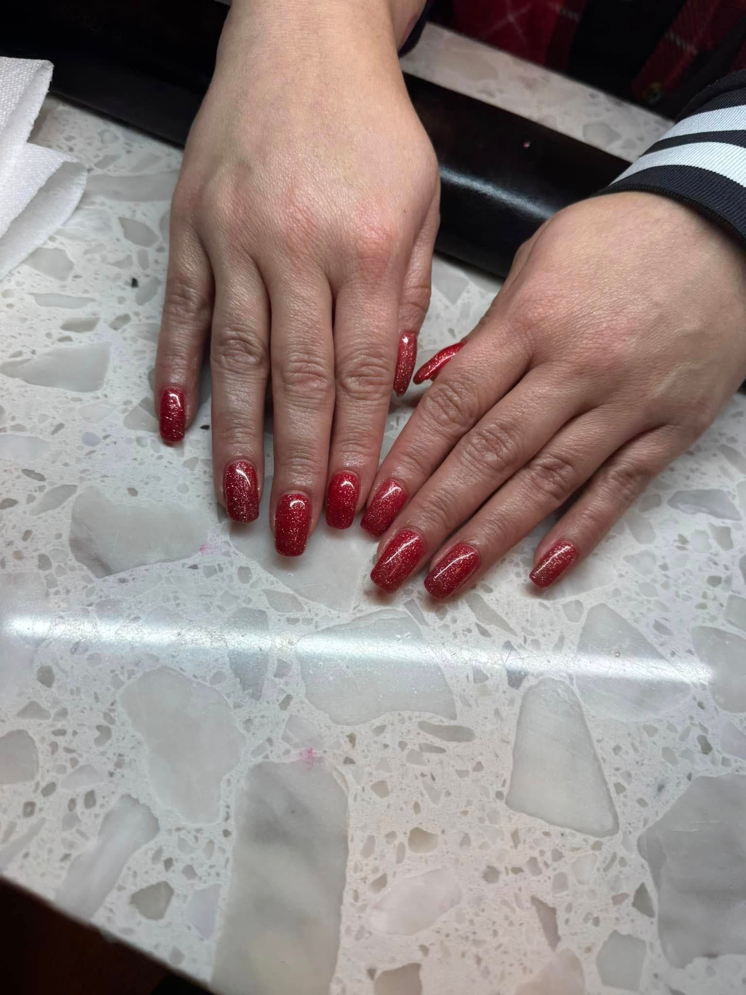 Hands with long, red glittery nails on a textured white surface.