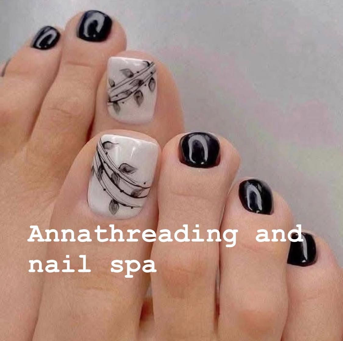 Pedicured toes with black polish on the majority, and white polish with leaf design on two big toes.