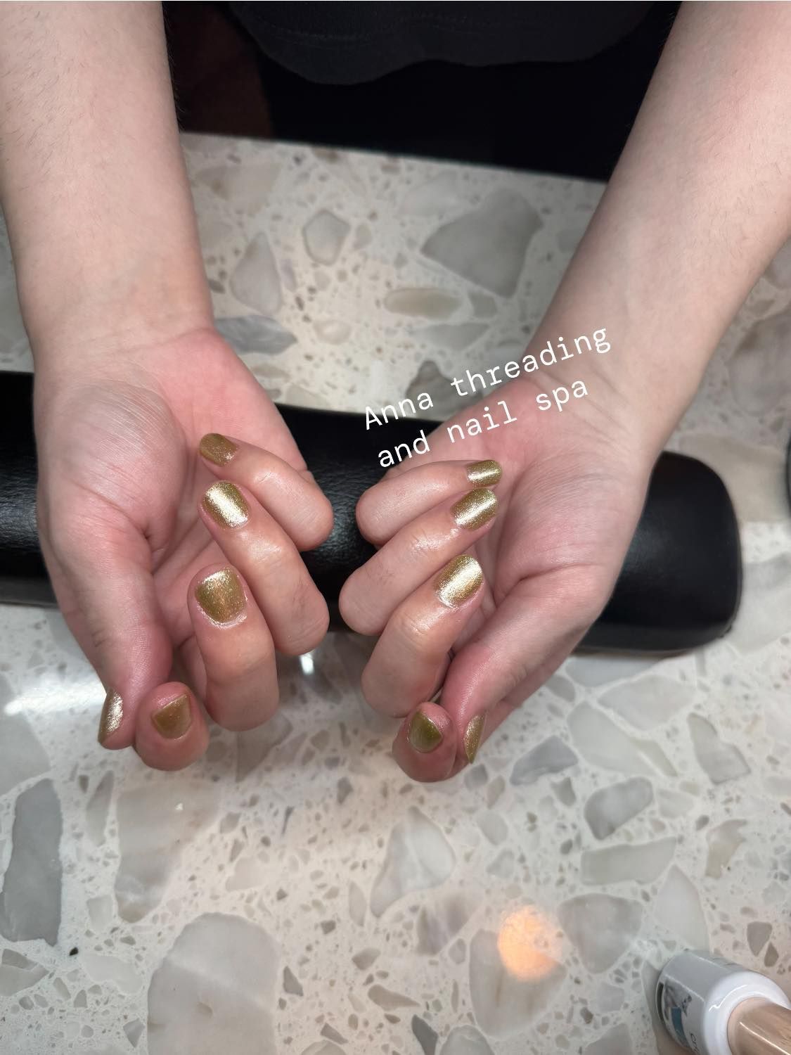 Hands with gold nail polish on a spa table at Anna threading and nail spa.
