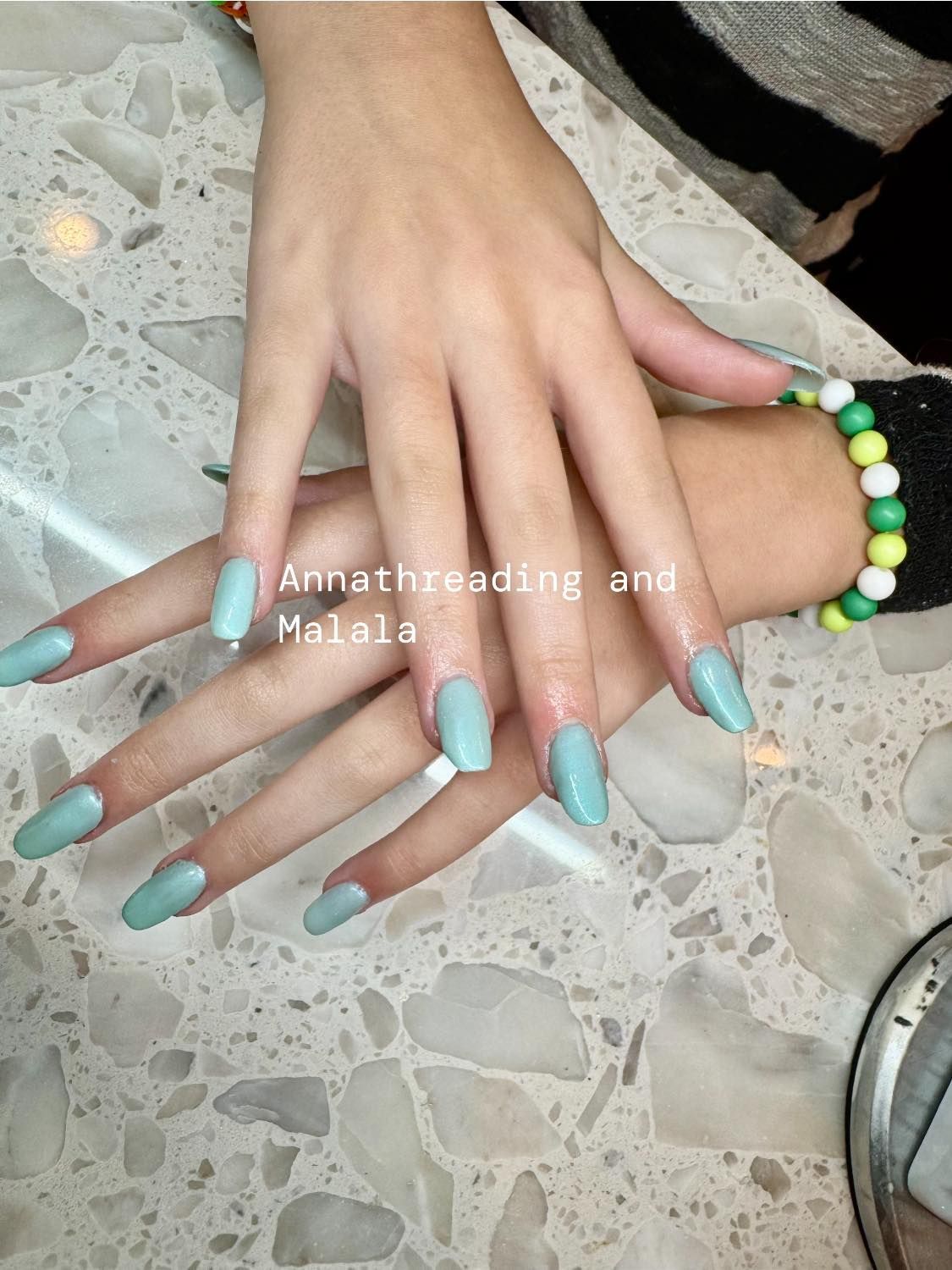 Hands with long, light blue painted nails resting on a textured, light-colored surface.
