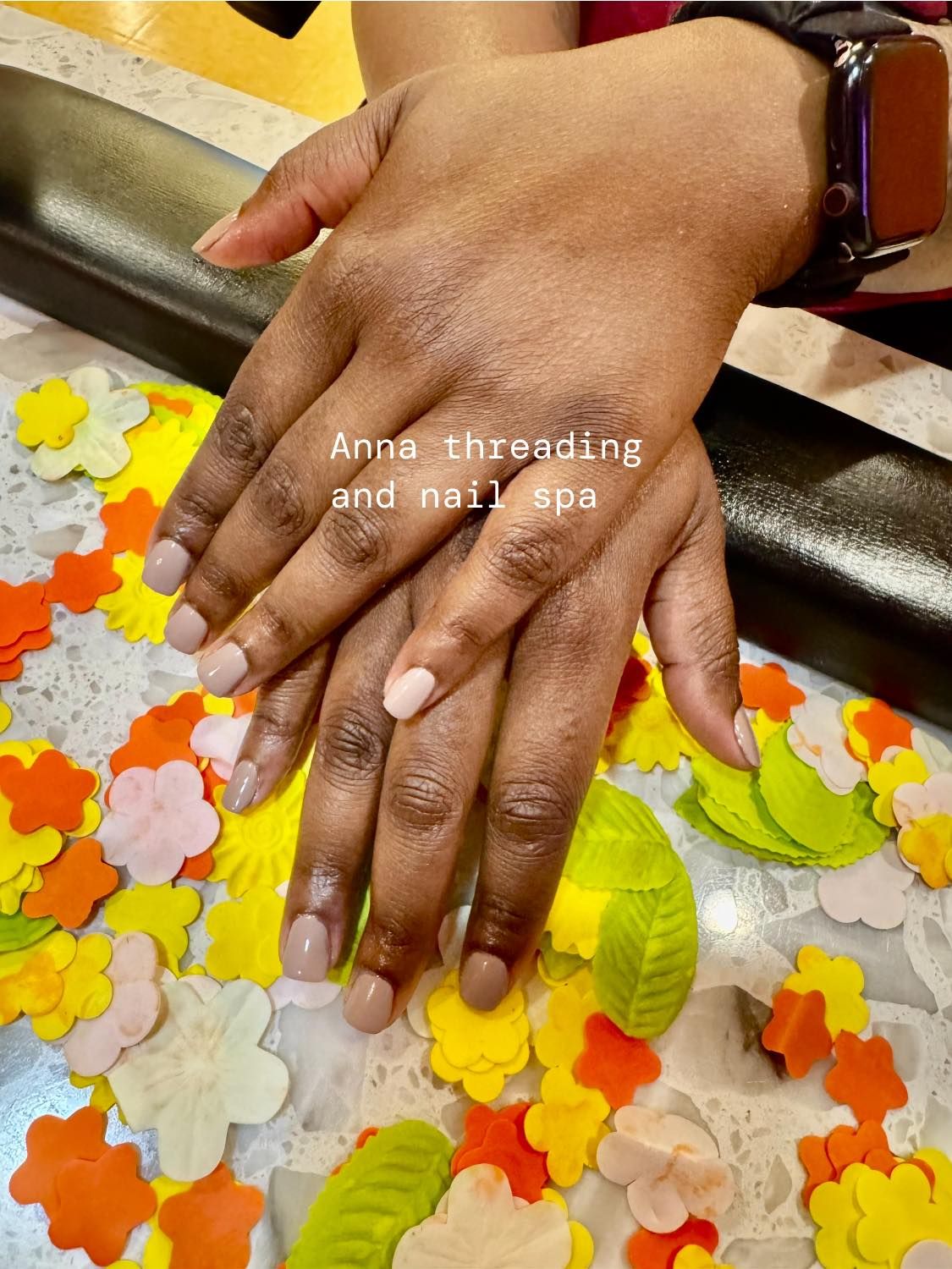 Hands with short, light brown nails, resting on a table with colorful paper flowers.