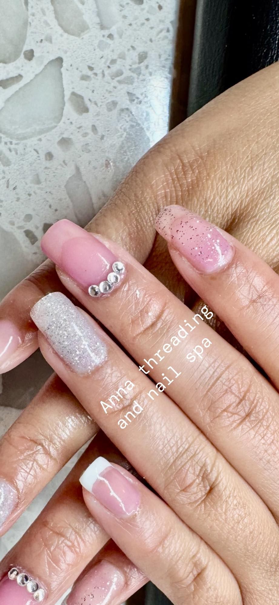 Woman's hand with pink and glitter nail polish. One nail has rhinestones and another has a french tip.