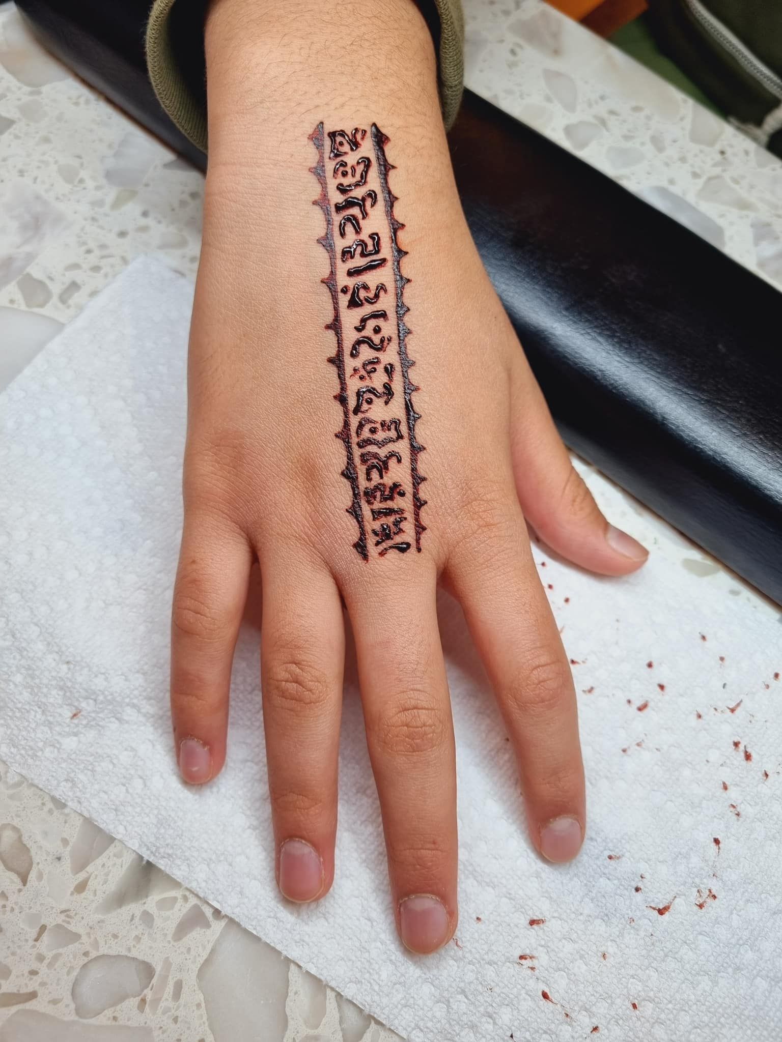Hand with a henna tattoo design of a rectangular strip on top, with a repeating pattern along the sides.