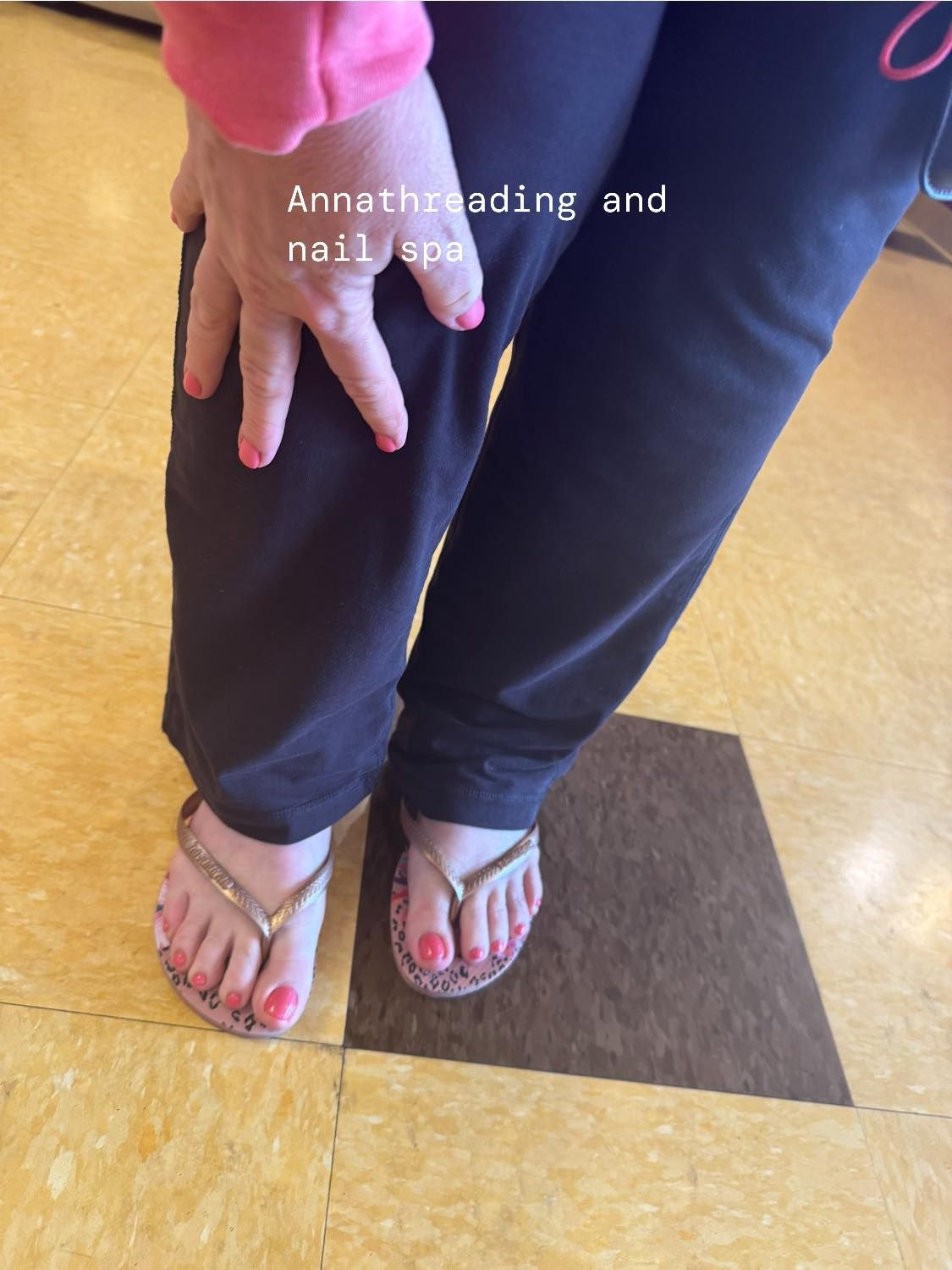 Person wearing pink nail polish, black pants, and sandals. Their foot is on a brown mat.