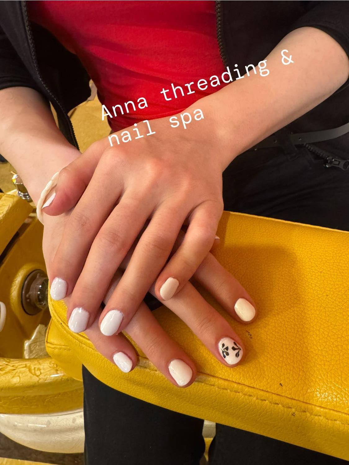 Person's hands with white, nude, and patterned nail polish, resting on a yellow surface, with text 