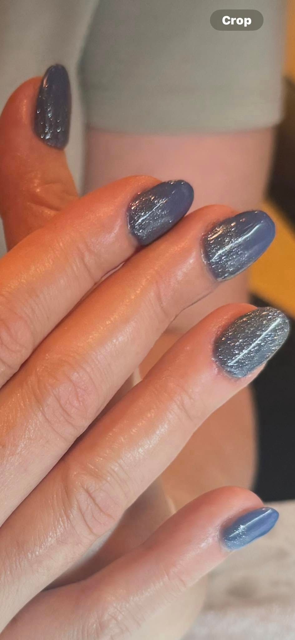Person's hand with blue nail polish, some with glitter.