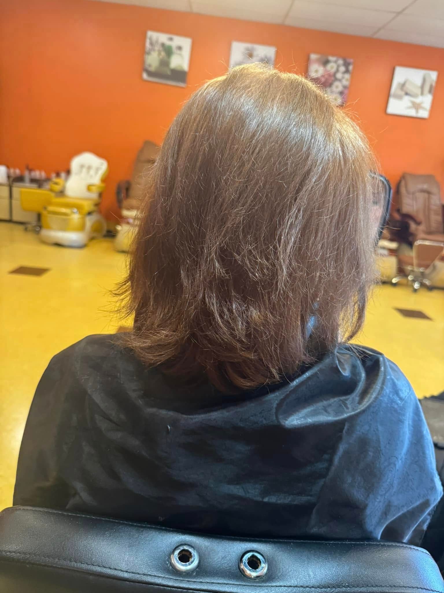 Person in a salon chair with brown hair. Orange wall in background with salon equipment.