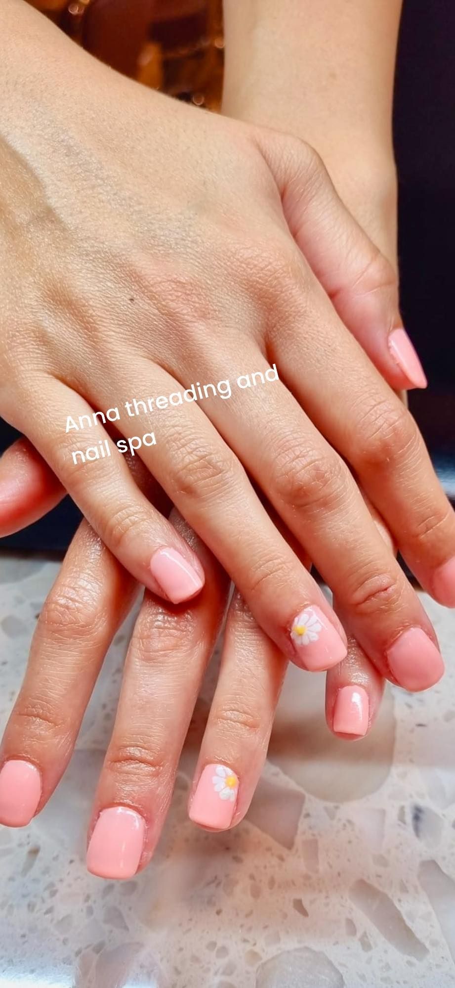 Hands with light pink square-shaped nails; two nails have small floral art.