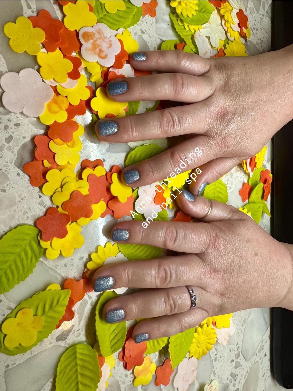 Hands with sparkly silver nails on a surface decorated with colorful leaves and flowers.