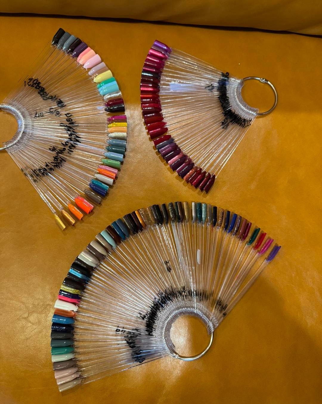 Three fan-shaped nail polish color swatches on a yellow surface, showcasing various shades.
