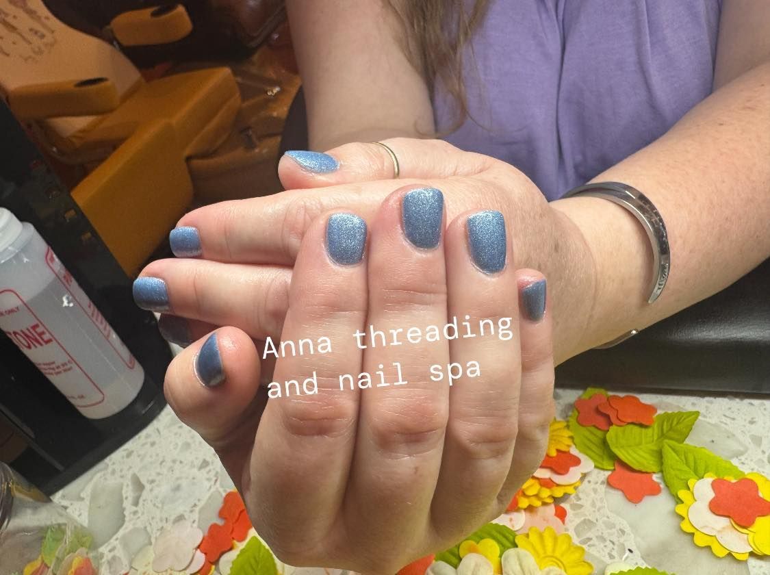 Hands with blue glitter nail polish at Anna Threading and Nail Spa.
