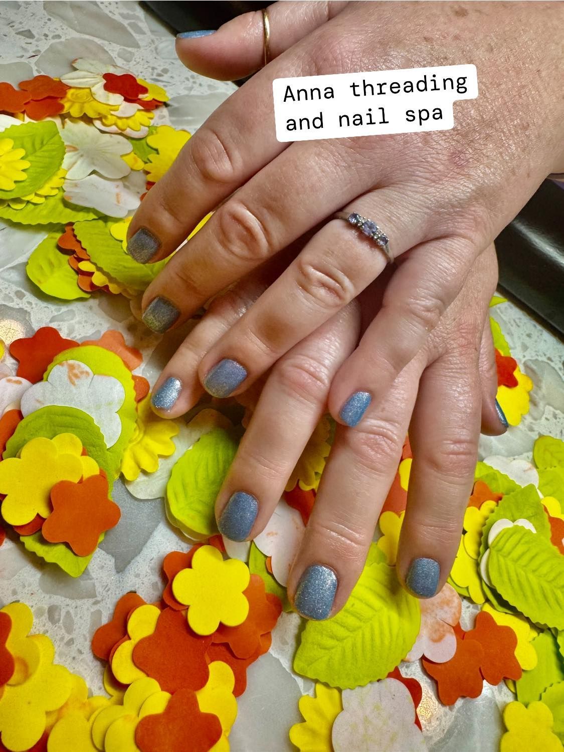 Hands with gray glitter nail polish, resting on colorful paper flower decorations. 