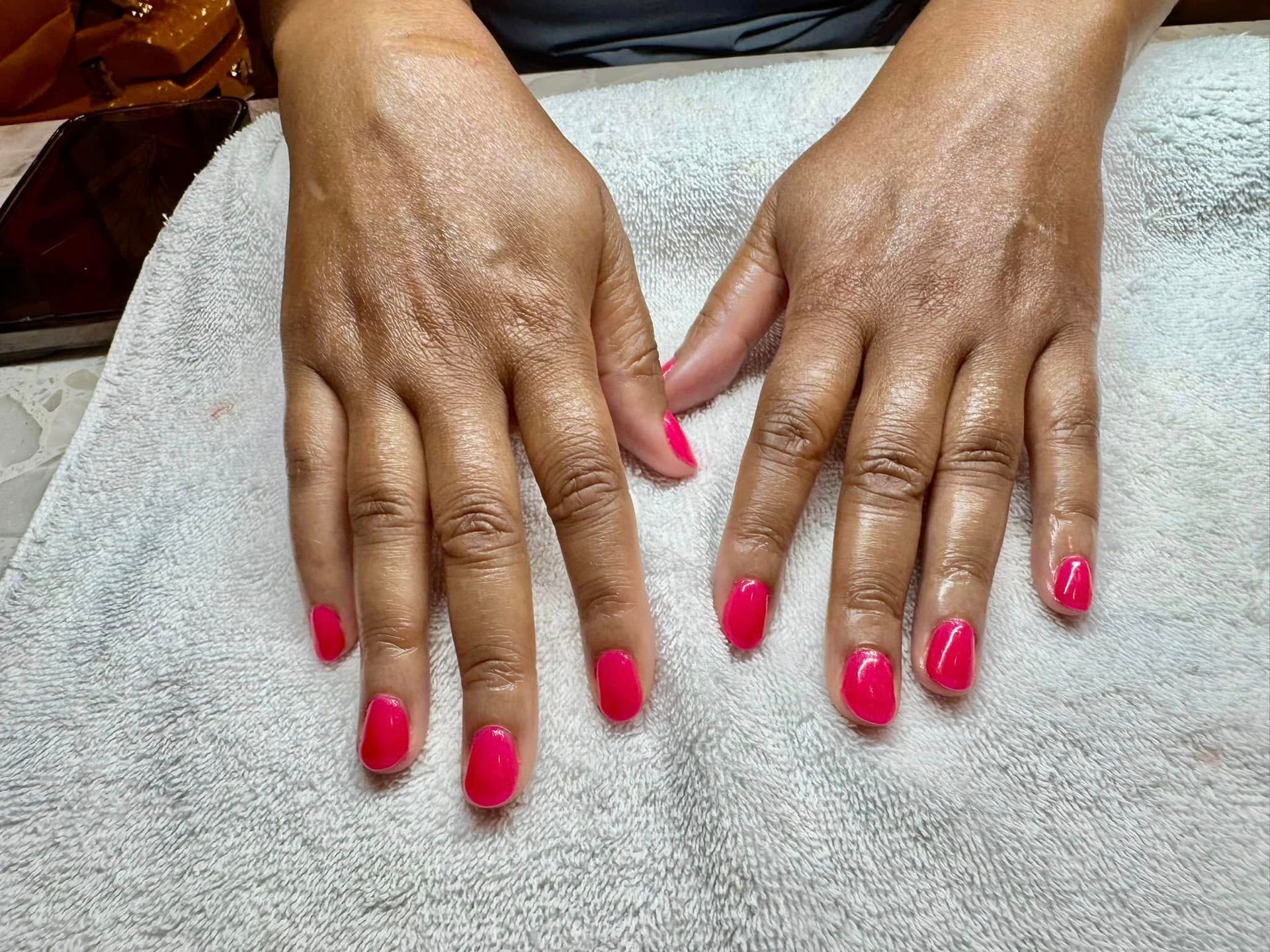Hands with freshly manicured nails in a bright pink color, resting on a light gray towel.