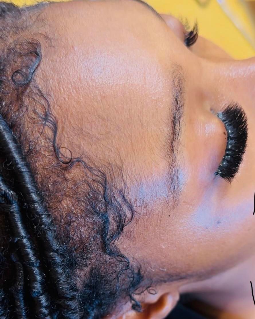 Close-up of a person's eye with thick, dark eyelash extensions and textured hair; yellow background.