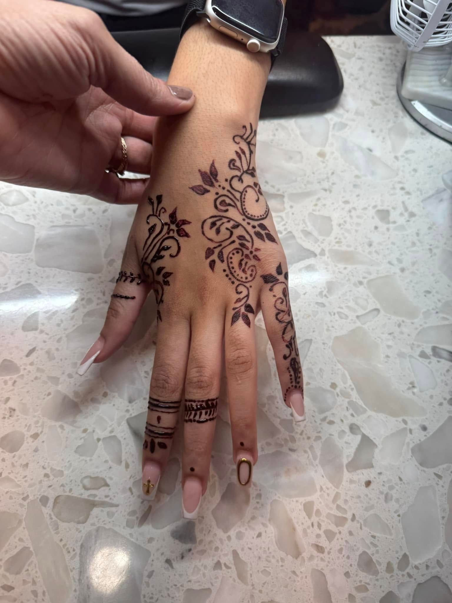 Hand with henna design, fingers with long nails, other hand touches wrist.