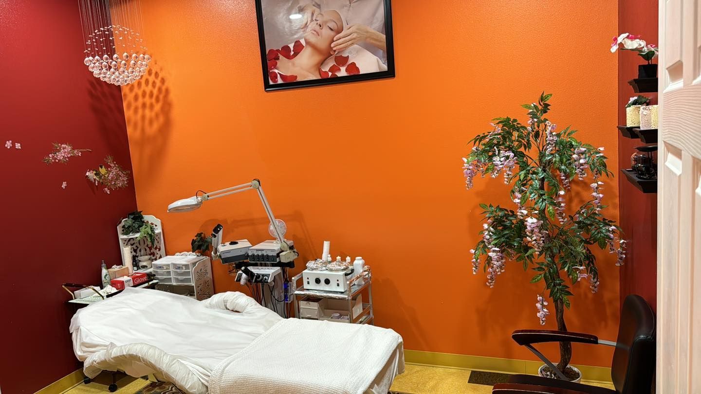 A facial treatment room with an orange and red walls, massage table, and decorative tree.