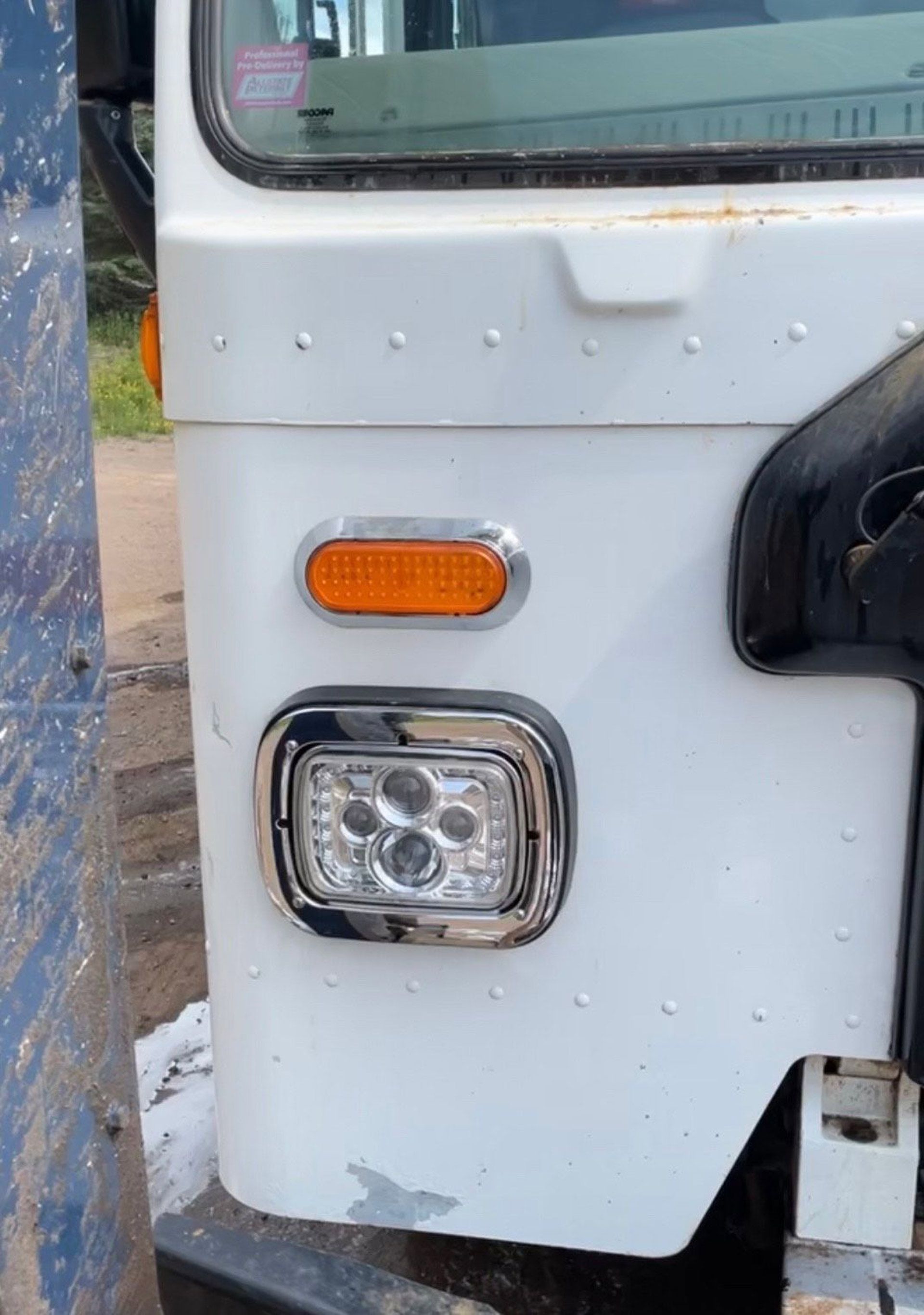 A white truck with a chrome headlight is parked on the side of the road.